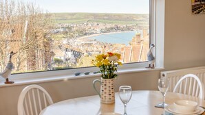 Ein Esstisch mit Stühlen, eine Vase mit Blumen und Blick auf eine Stadt und einen Fluss durch ein Fenster.