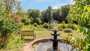 Un jardin agrémenté d’une fontaine, d’un banc en bois et d’une végétation luxuriante.