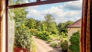 Une vue à travers une fenêtre sur un jardin, avec un chemin menant à un bâtiment.