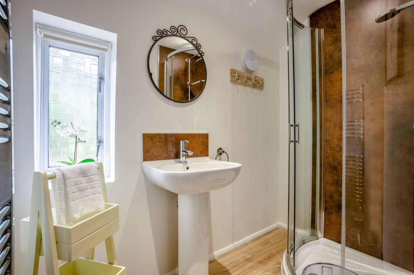 A bathroom with a white sink, a round mirror, a towel rack, and a glass shower enclosure.