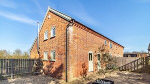 A brick building with a sloped roof, a small garden area with a tree, and a gravel driveway. - 3 Bed in Knodishall (oc-wbco) (Knodishall)
