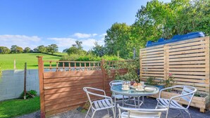 A patio with a round glass table and four metal chairs, surrounded by a wooden fence and a wooden wall.