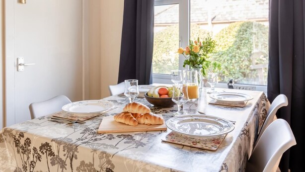 A dining table set with plates, glasses, a bowl of fruit, croissants, and a pitcher of orange juice.