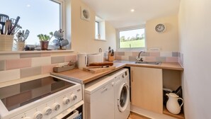 A compact kitchen with a stove, oven, and washing machine, a sink, and a window with a view of the outdoors.