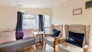 A cozy living room with a sofa, two armchairs, a small table, and a window with curtains.