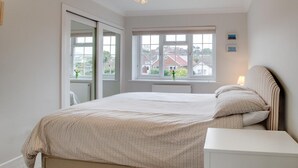 Ein Schlafzimmer mit Bett, Nachttisch, Fenster mit Blick und einer Tür zu einem weiteren Raum.