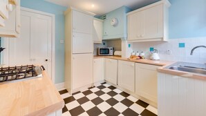 A kitchen with white cabinets, a microwave, a gas stove, and a checkered floor. - 3 Bed in Southwold (oc-sl139) (Southwold)