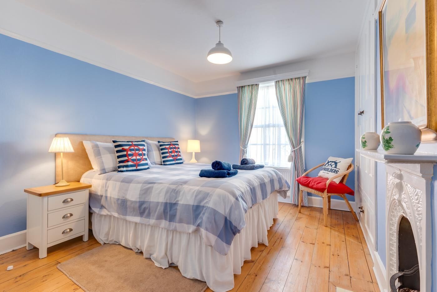 Une chambre à coucher avec un lit, des tables de chevet, une chaise, une cheminée et une fenêtre avec des rideaux.