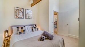 Un dormitorio con una cama, dos obras de arte en la pared, una lámpara de noche y una puerta que da a otra habitación.
