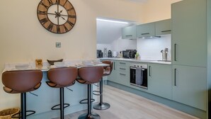 Una cocina moderna con barra, que incluye un reloj de pared grande, taburetes de bar y muebles de cocina de color claro.