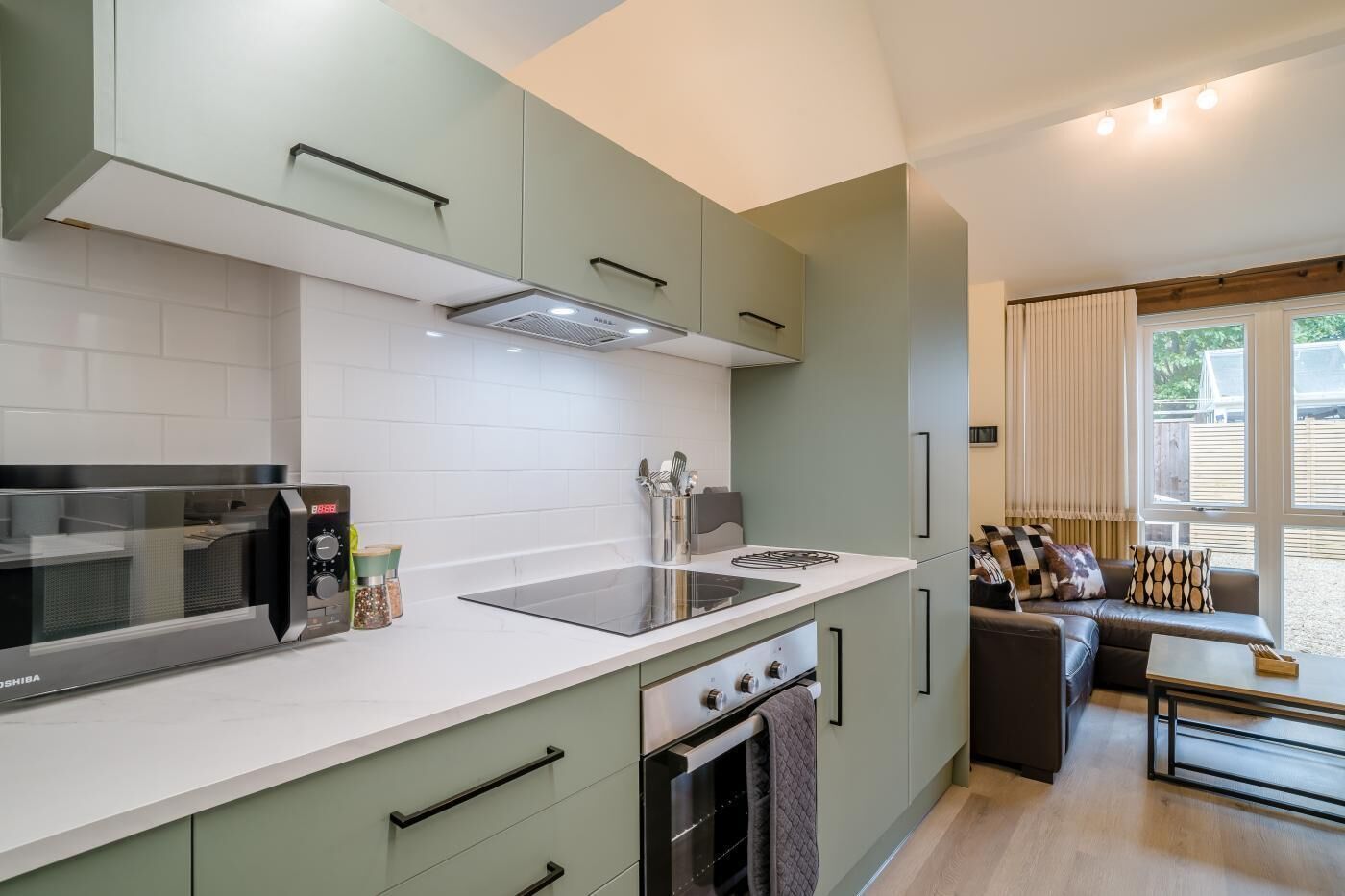 A modern kitchen with a built-in microwave, stove, and sink. There is a dining area with a table and chairs, and a window offering a view of the outdoors.