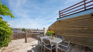 Eine Holzterrasse mit Tisch und Stühlen, ein Holzzaun und ein Blick auf die Stadt im Hintergrund.