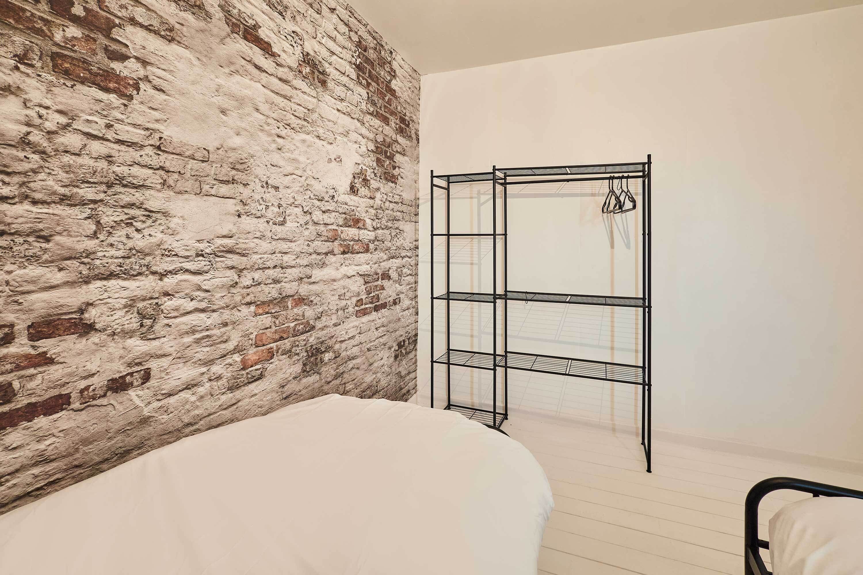 A room with a brick wall, a metal shelving unit, and a bed with white bedding.