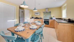 A modern kitchen with wooden cabinets, a central island, and blue pendant lighting. - 6 Bed in Knodishall (oc-bil) (Knodishall)