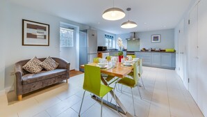 A modern kitchen with a dining area, featuring a sofa, dining table, chairs, pendant lights, and cabinets. - 6 Bed in Knodishall (oc-bil) (Knodishall)