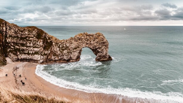 A coastal landscape with a prominent rock arch formation, a sandy beach, and the ocean. - 4 Bed in Bere Regis (oc-g33051) (Bere Regis)