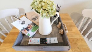 Una bandeja con un control remoto, un libro, un florero con flores y un candelabro sobre una mesa de madera.