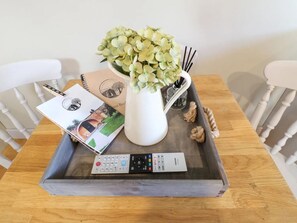 A tray with a remote control, a book, a vase with flowers, and a candle holder on a wooden table.