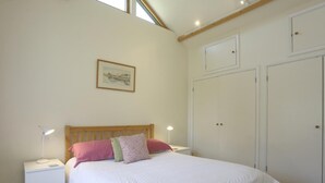 Ein Schlafzimmer mit hölzernem Kopfteil, weißem Bettbezug, zwei Nachttischlampen, einem gerahmten Bild an der Wand und einem zweitürigen Kleiderschrank.