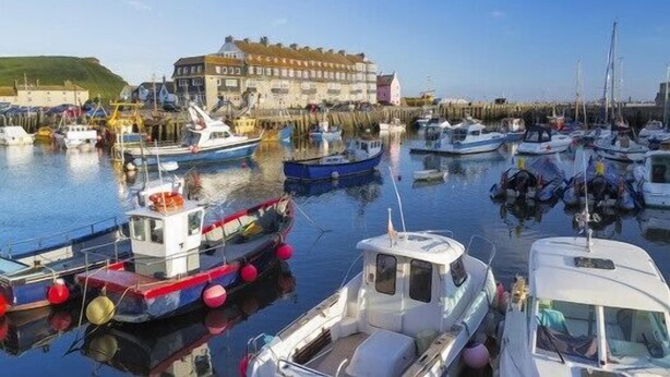 A marina with various boats docked, a building with a distinct architectural style, and calm water reflecting the boats. - 1 Bed in West Bay (oc-wy537) (West Bay)