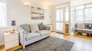 A modern living room with a grey sofa, a coffee table, a lamp, and a painting on the wall. - 1 Bed in West Bay (oc-wy537) (West Bay)