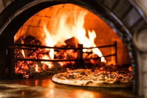 En pizzaovn med ild indeni, en pizza på disken og en murstensvæg.