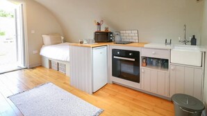 Ett kompakt kök med mikrovågsugn, ugn och diskho, ett litet kylskåp och en säng i ett sovloft.
