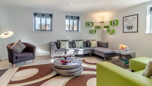 Ein modernes Wohnzimmer mit einem grauen Sofa, einem runden Couchtisch und einem grünen Sessel.