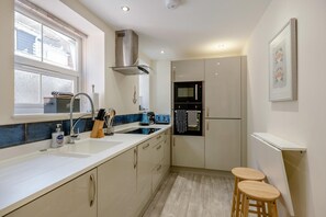A modern kitchen with a sink, stove, and two stools.