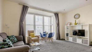 A living room with a sofa, armchair, dining table, chairs, a TV, and a bookshelf.