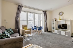 A living room with a sofa, armchair, dining table, chairs, a TV, and a bookshelf. - 1 Bed in Weymouth (oc-wy437) (Weymouth)