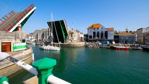 A harbor with boats, a green bridge, and buildings including one with 'RENDEZVOUS' sign.