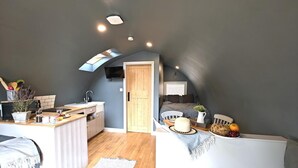 Une chambre compacte dotée d’une kitchenette, d’une armoire intégrée, d’un petit coin salon et d’une porte donnant sur une autre pièce.