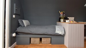 Une petite chambre comprenant un lit, un coin cuisine et deux paniers placés sous le lit.