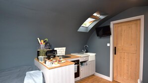 A compact kitchen with a built-in oven, a microwave, and a sink. There's a wooden door and a small window above the sink. - 1 Bed in Rocester (oc-o33055) (Barrow Hill)
