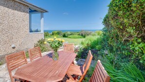 Een houten tafel met zes stoelen, een vaas met gele bloemen en uitzicht op zee.