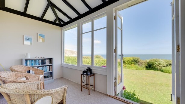 Een kamer met een groot raam, rieten stoelen, een boekenkast en een telescoop.