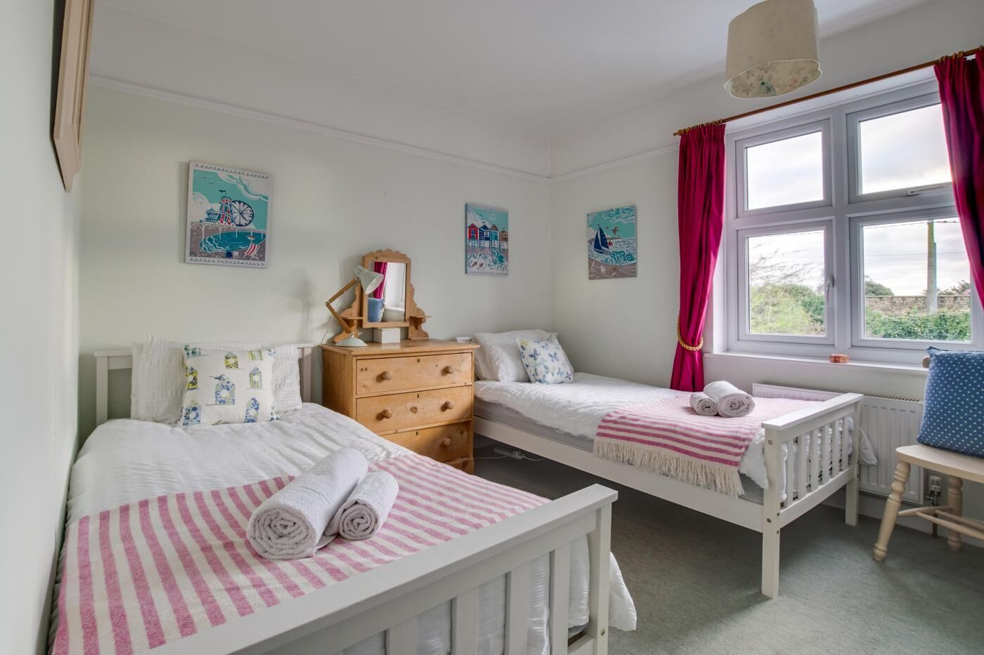 A bedroom with two single beds, a dresser, a window with curtains, and wall art.