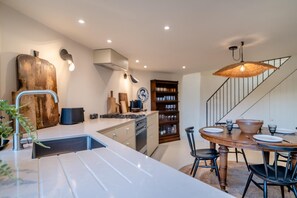 A modern kitchen with a central island, built-in oven, and a dining area with a wooden table and chairs. - 3 Bed in Winfrith Newburgh (oc-w33007) (Winfrith Newburgh)