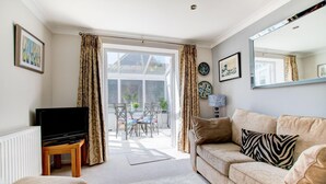 A living room with a sofa, a TV, a coffee table, a dining table with chairs, and a large window with curtains. - 2 Bed in Swanage (oc-wy552) (Swanage)