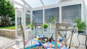 A conservatory with a glass table, chairs, and potted plants. - 2 Bed in Swanage (oc-wy552) (Swanage)