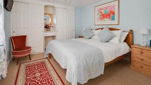 Ein Schlafzimmer mit einem Bett, einem Sessel, einer Kommode, einem Spiegel, einem Gemälde und einem Fernseher.