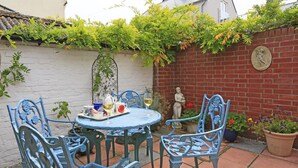 Eine Terrasse mit einem runden Tisch, blauen Metallstühlen und einer Statue einer Frau.