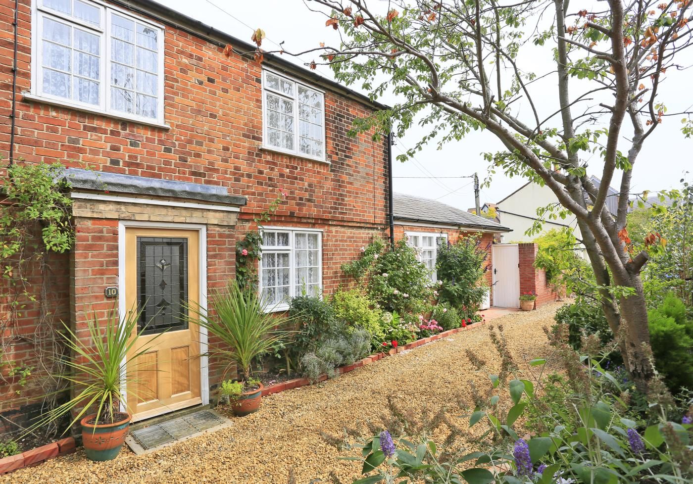 A two-story brick house with a front garden, a wooden door, and a visible number '10' on the wall.
