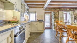 Una cocina con armarios blancos, encimera negra y pared de piedra.