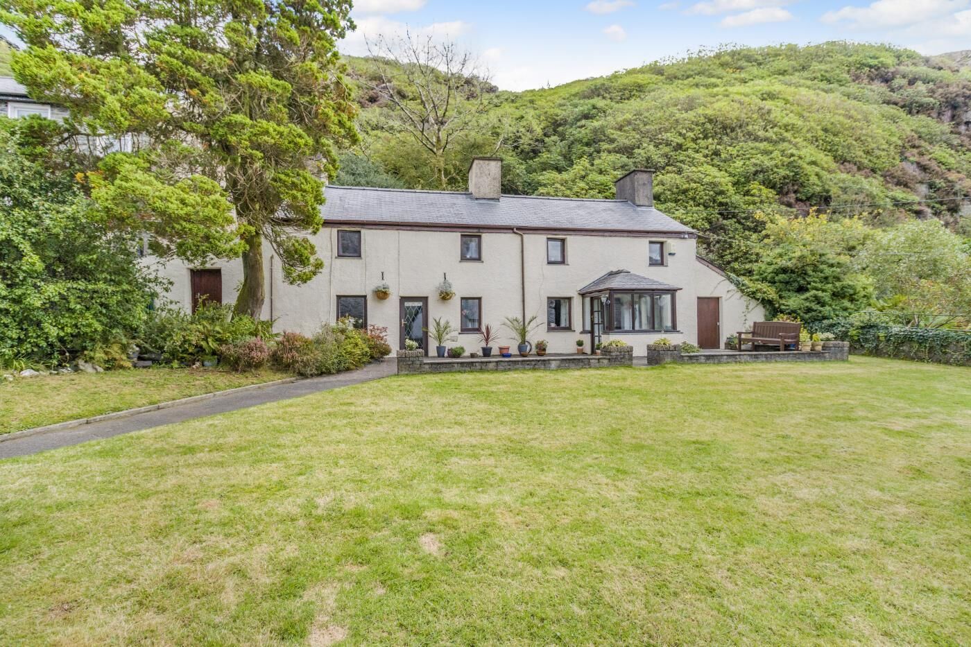 A two-story house with a large front lawn, a conservatory, and a stone wall.