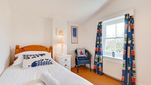 Een slaapkamer met een bed, nachtkastje, stoel, raam en gordijnen.