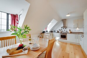 A modern kitchen with white cabinets, a wooden dining table, and a large window. - 3 Bed in Swanage (oc-wy269) (Swanage)