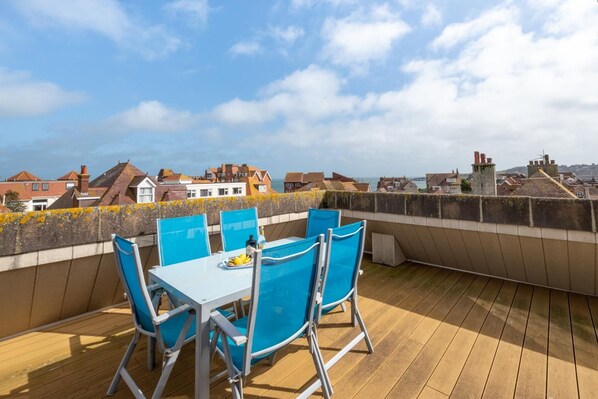 A rooftop terrace with a table and chairs, overlooking a coastal town. - 3 Bed in Swanage (oc-wy269) (Swanage)