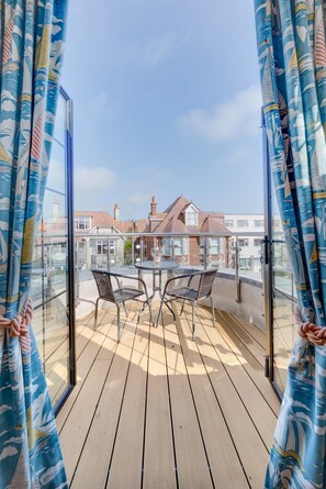 A balcony with a table and chairs, a glass railing, and a view of houses in the background. - 3 Bed in Swanage (oc-wy269) (Swanage)
